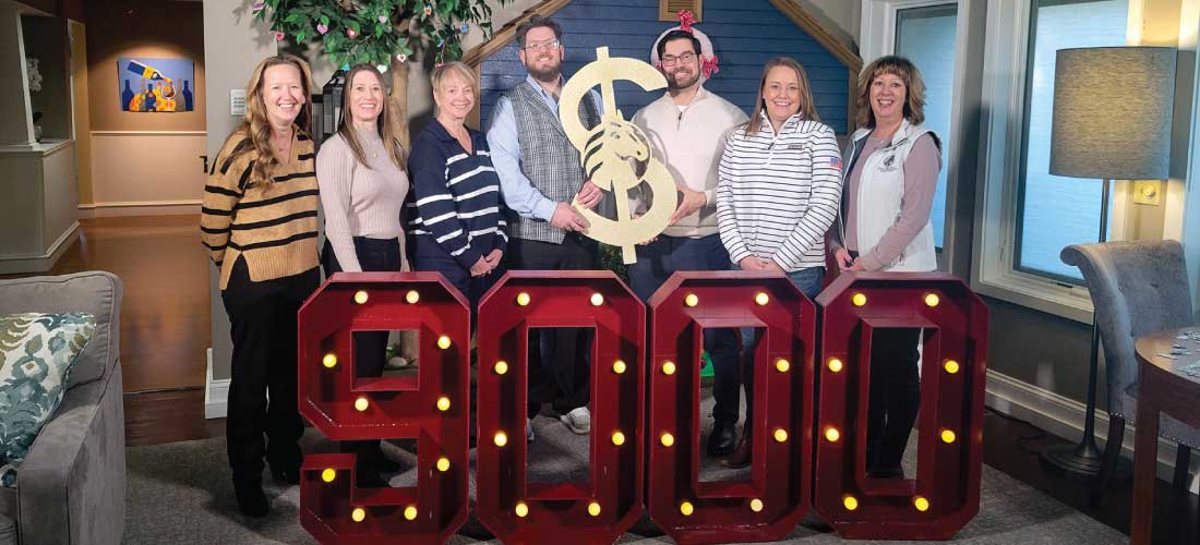 Group of people at Ronald McDonald House posing behind "9,000" marquee numbers.