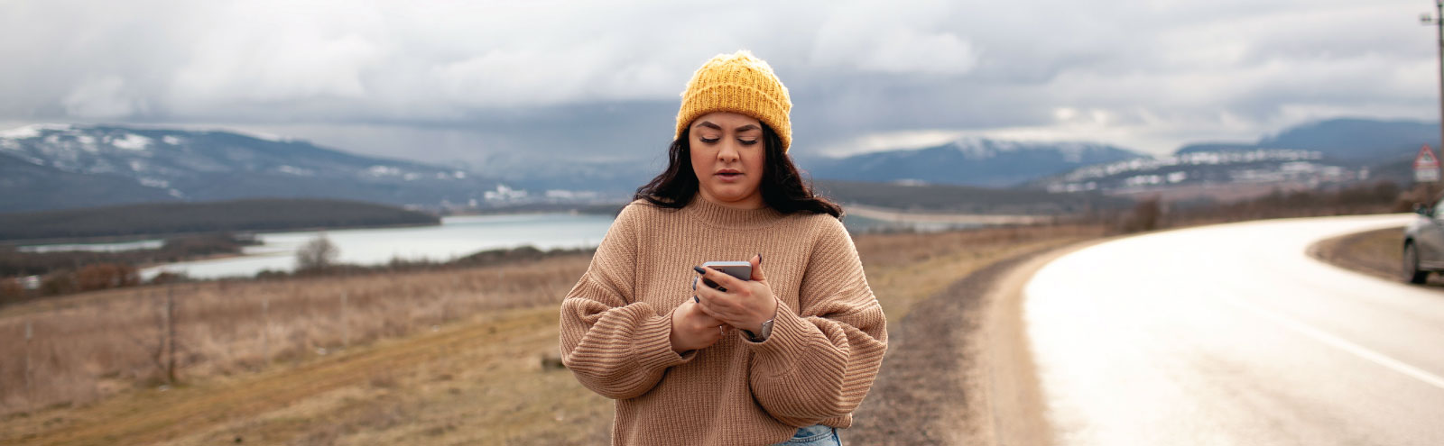 Woman walking along a rural mountain road with a cell phone.