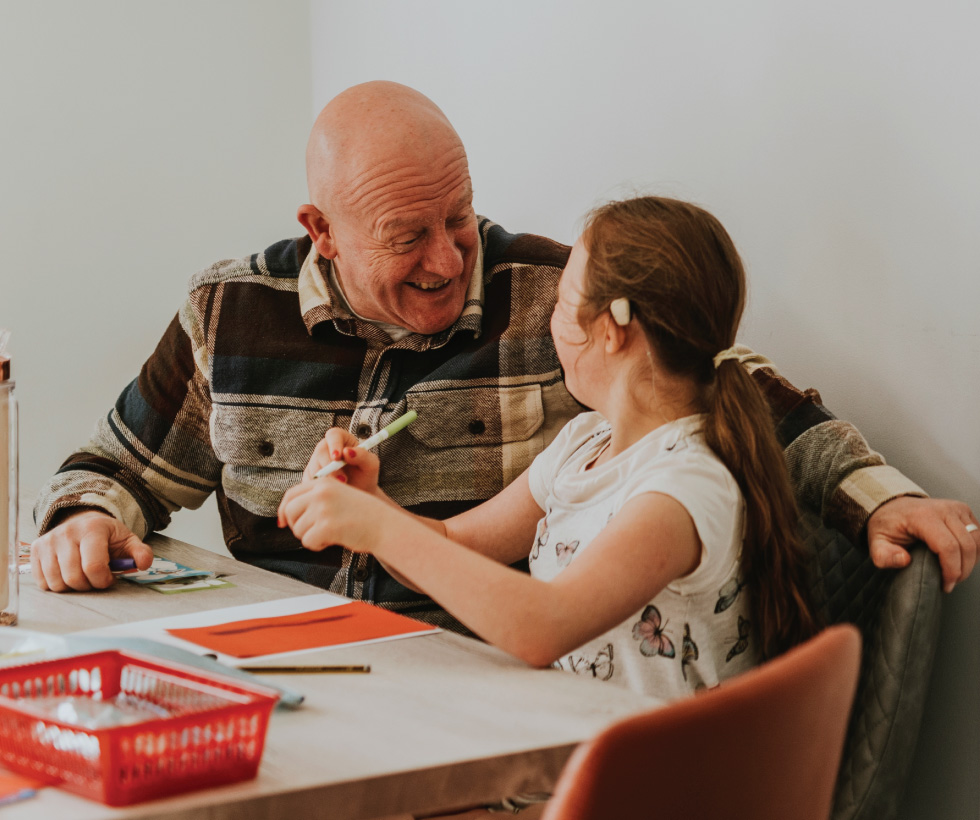 Grandfather and granddaughter sitting at a table laughing together.