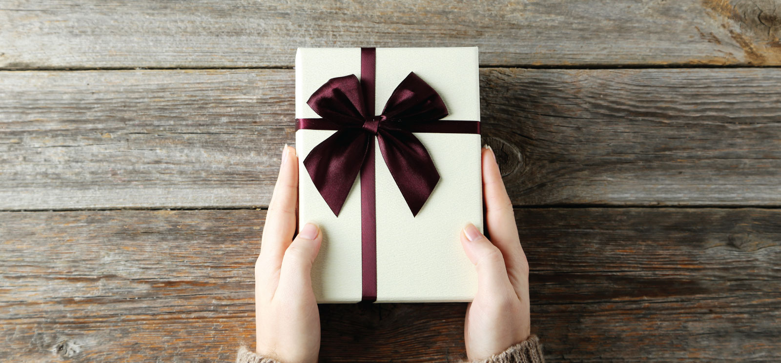 Hands holding a gift box with a burgundy  bow