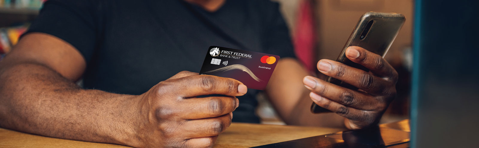 Man holding a First Federal business debit card and mobile phone.